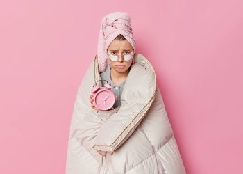 upset-young-pretty-woman-frowns-face-looks-displeased-wears-towel-head-wrapped-blanket-holds-alarm-clock-awakes-early-morning-applies-beauty-patches-eyes-poses-indoor-pink-wall (1)